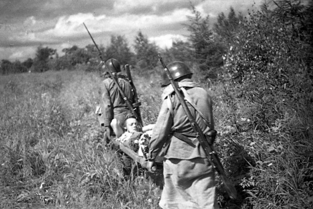 Санитары 165-го стрелкового полка  79-й стрелковой дивизии 16-й армии Дальневосточного фронта: санитар санитарной роты Мария Васильевна Грибанова (1923 – 2010 гг.) и санитар санитарного взвода 3-го стрелкового батальона младший сержант Зинаида Сергеевна Иванова (1924 г.р.) выносят раненого с поля боя. Южный Сахалин , префектура Карафуто. Япония. Август 1945 г. Фотограф: Григорий Соколов.